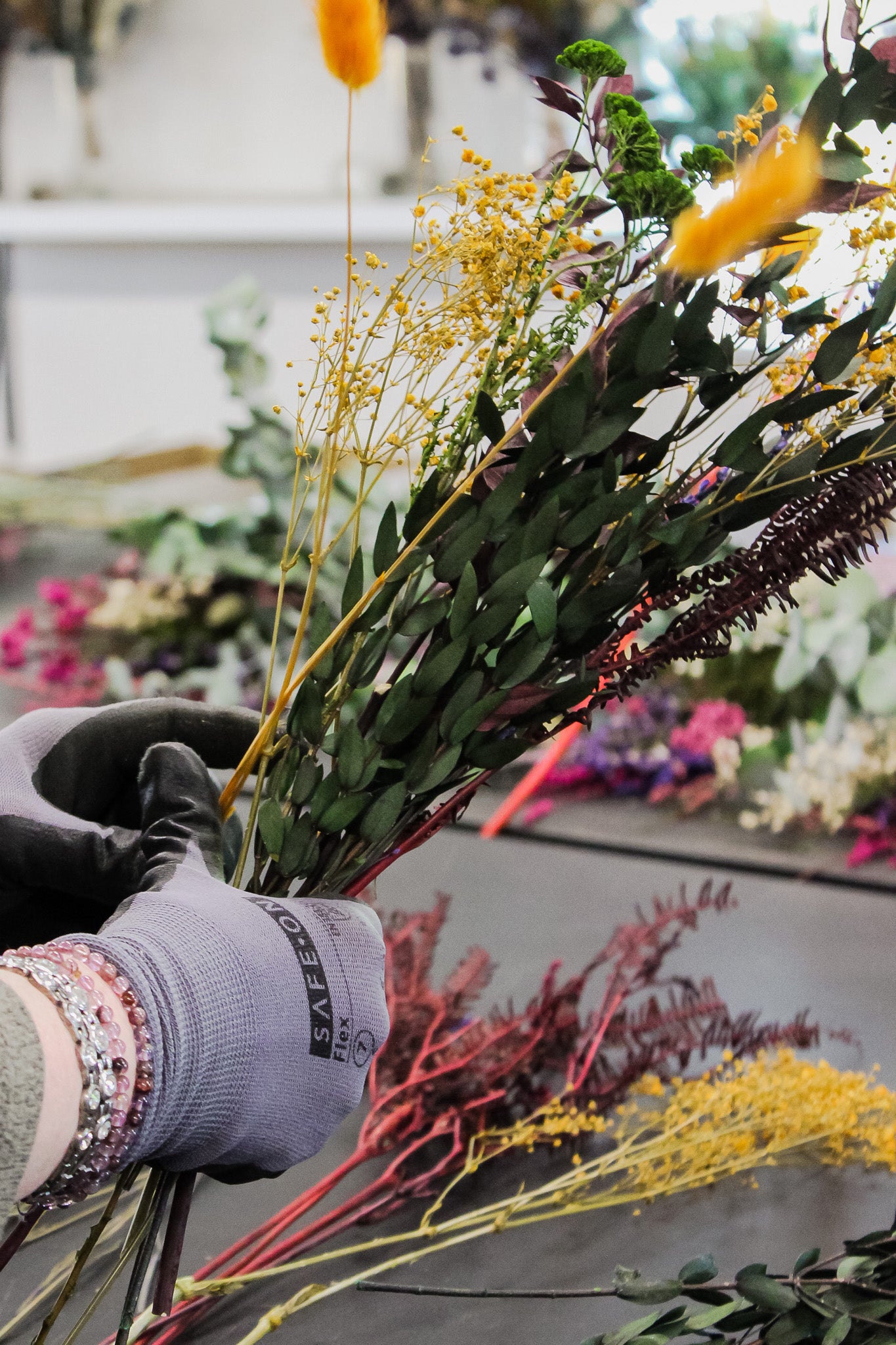 Händer i arbetshandskar arrangerar och binder en blombukett, närbild.