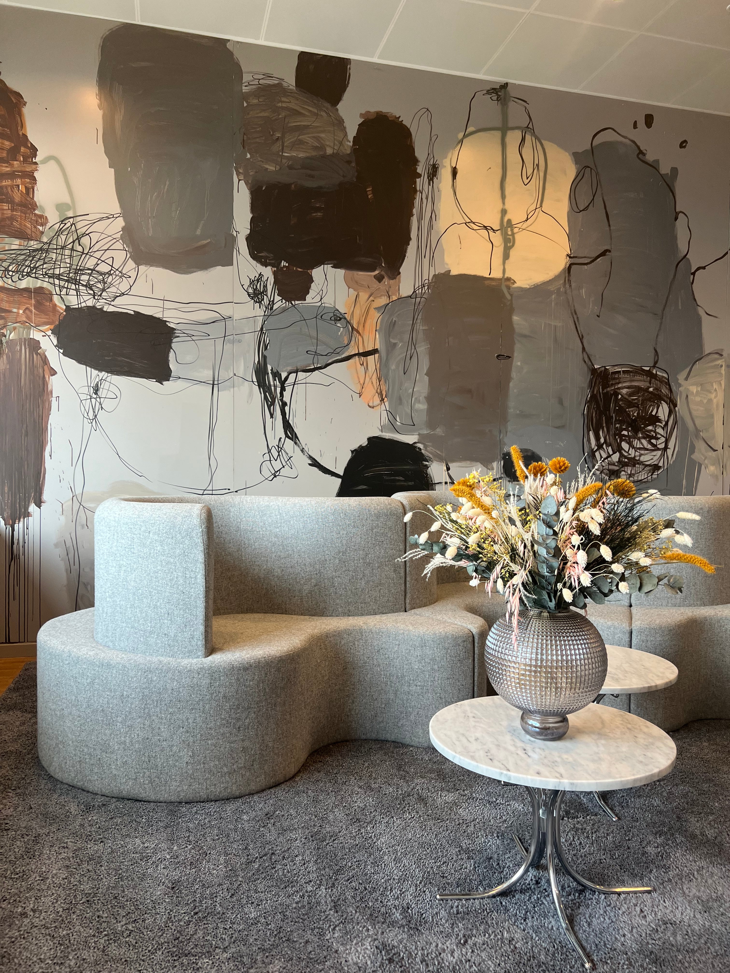Lounge miljö med soffor och små runda bord. En vacker bukett i orange, vitt och grönt pryder ett av borden