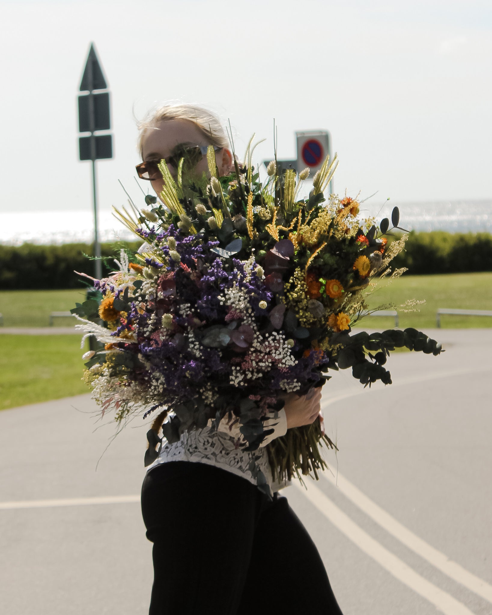 Utomhus bild av ung kvinna med solglasögon som håller fyra olika buketter tillsammans som en enda stor blombukett.