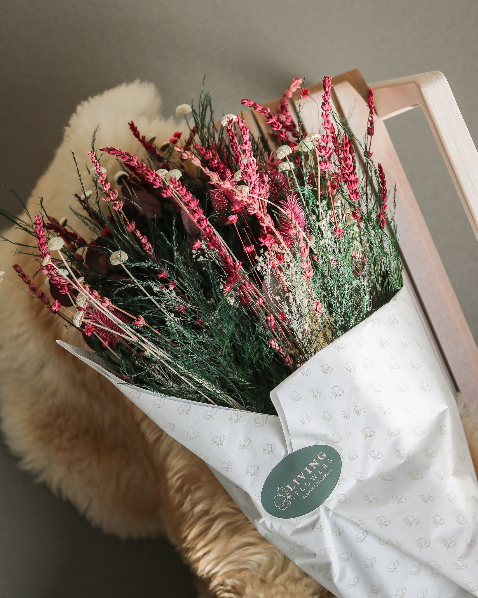 På en stol ligger en blomsterbuket i røde nuancer med hvide highlights, indpakket i silkepapir.