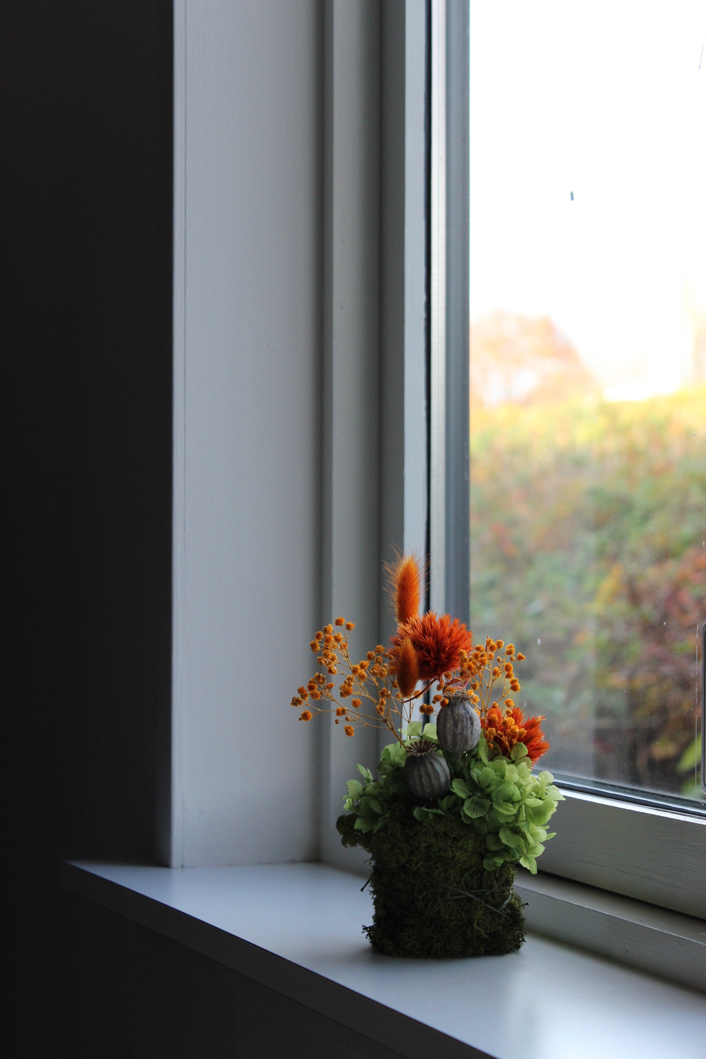 En lille, farverig dekoration med langtidsholdbare blomster står i vindueskarmen.