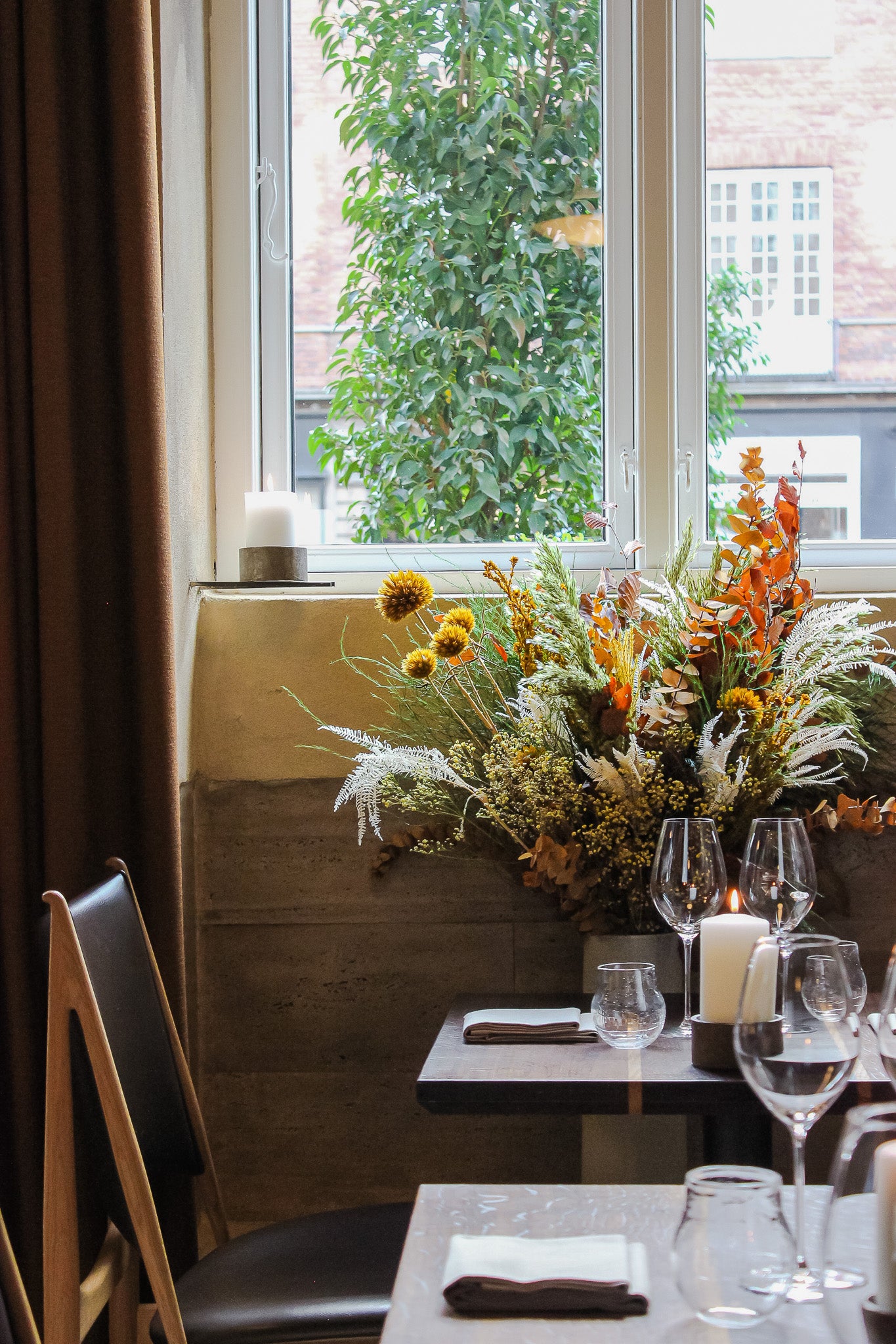 I en restaurant står en imponerende blomsterbuket i varme efterårsfarver foran vinduet.